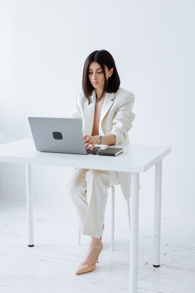 Businesswoman in a white suit working on a laptop in a minimalist office setting.